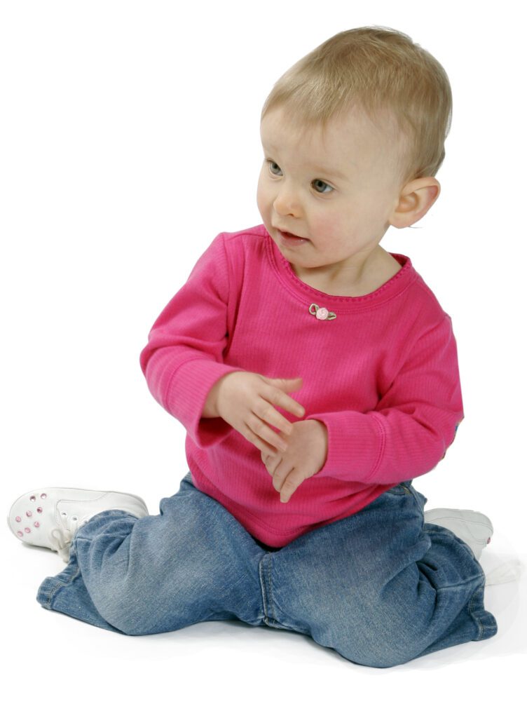 A baby in a pink shirt is sitting on the floor, engaging in social play.