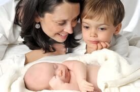 Mother with newborn baby and older sibling sharing a bonding moment