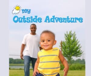 Smiling toddler in a yellow shirt enjoys the outdoors with an adult in the background, promoting the Baby Signs® My Outside Adventure class.