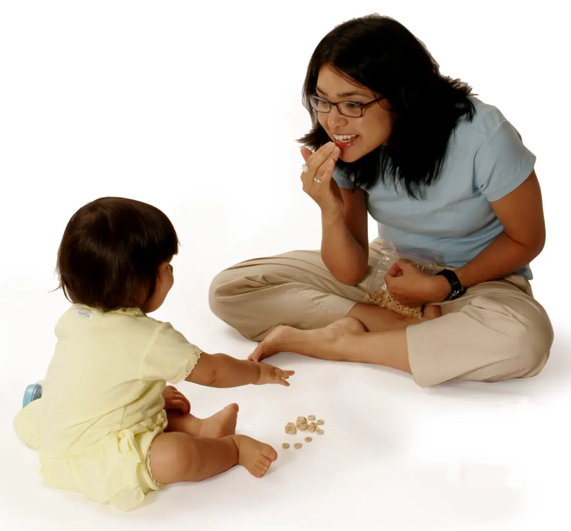 Parent and baby sitting together during snack time, using early signing to communicate with pieces of cereal on the floor.